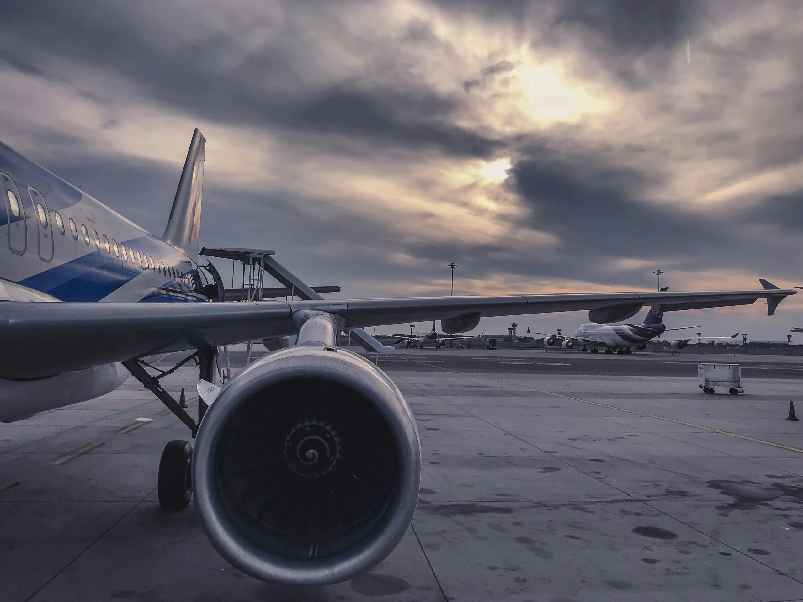 A passenger airplane is parked on the tarmac at sunset, with another aircraft in the background.